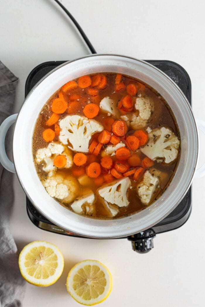 Carrots and cauliflower cooking in broth in a soup pot.