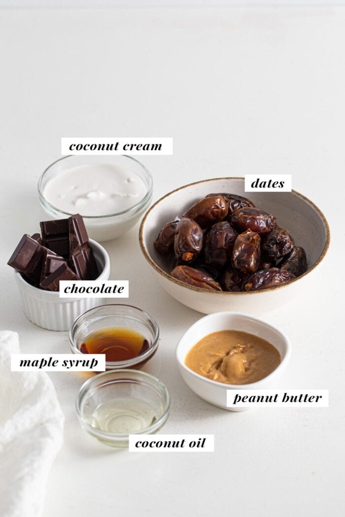 Dates, chocolate, peanut butter, coconut cream and maple syrup labelled in small glass dishes.