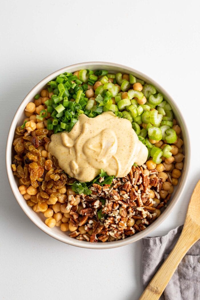 Walnuts, raisins, celery and chickpeas in a large salad bowl topped with a creamy yogurt dressing.