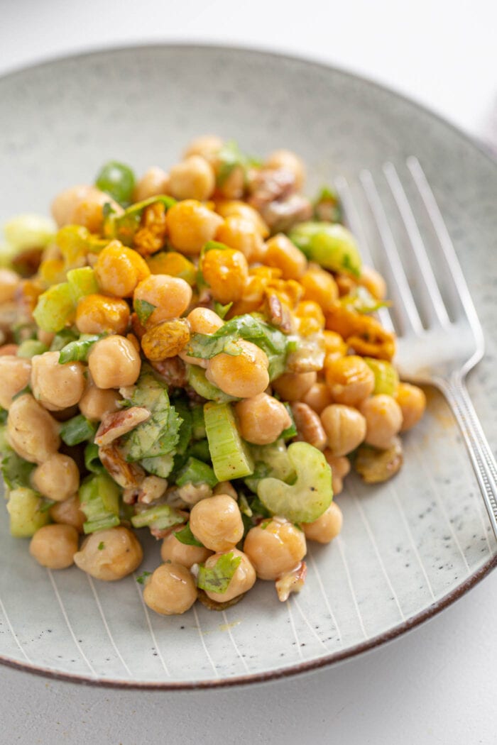 Close up of a curried chickpea salad with celery, walnuts and raisins on a plate.