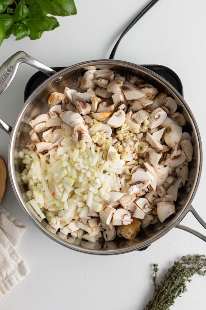 Diced mushrooms, onion and garlic cooking in a skillet on a small induction cooktop.