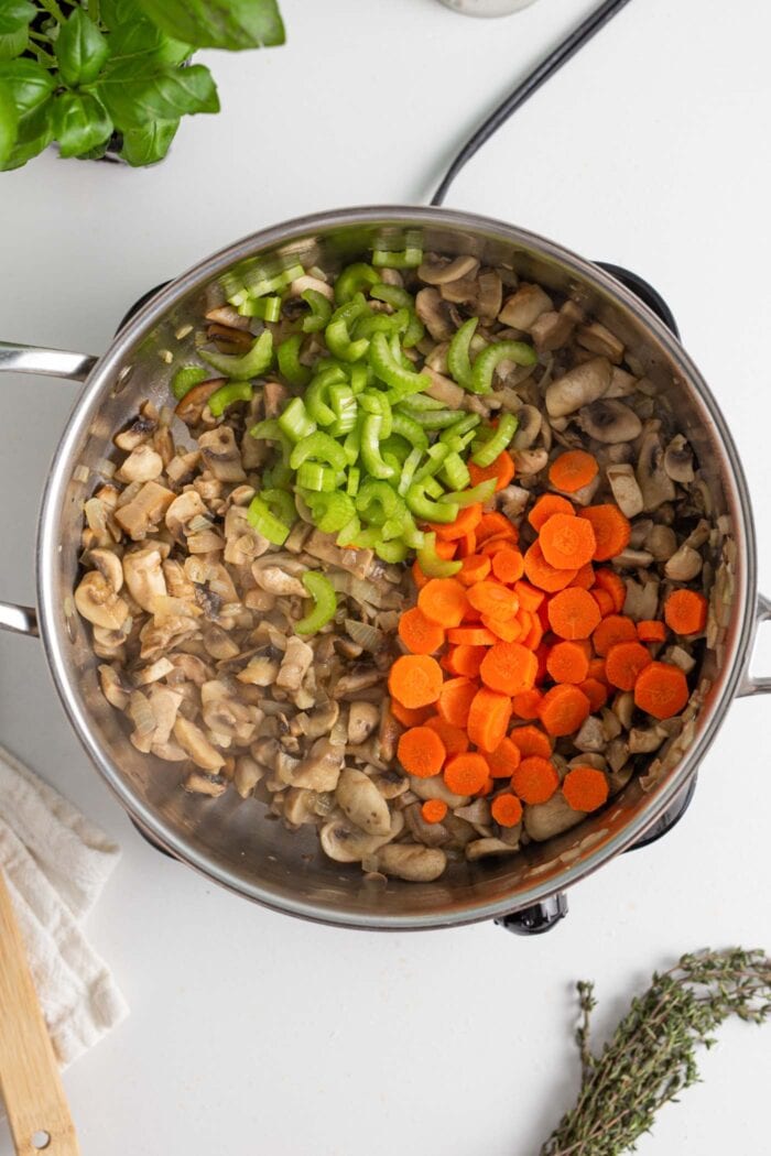 Diced carrots and celery in a skillet with cooked mushrooms.