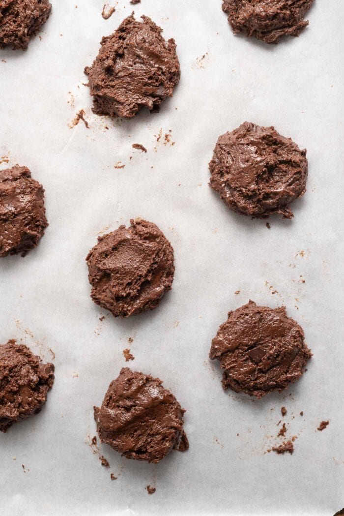 Unbaked chocolate cookies on. a baking tray lined with parchment paper.