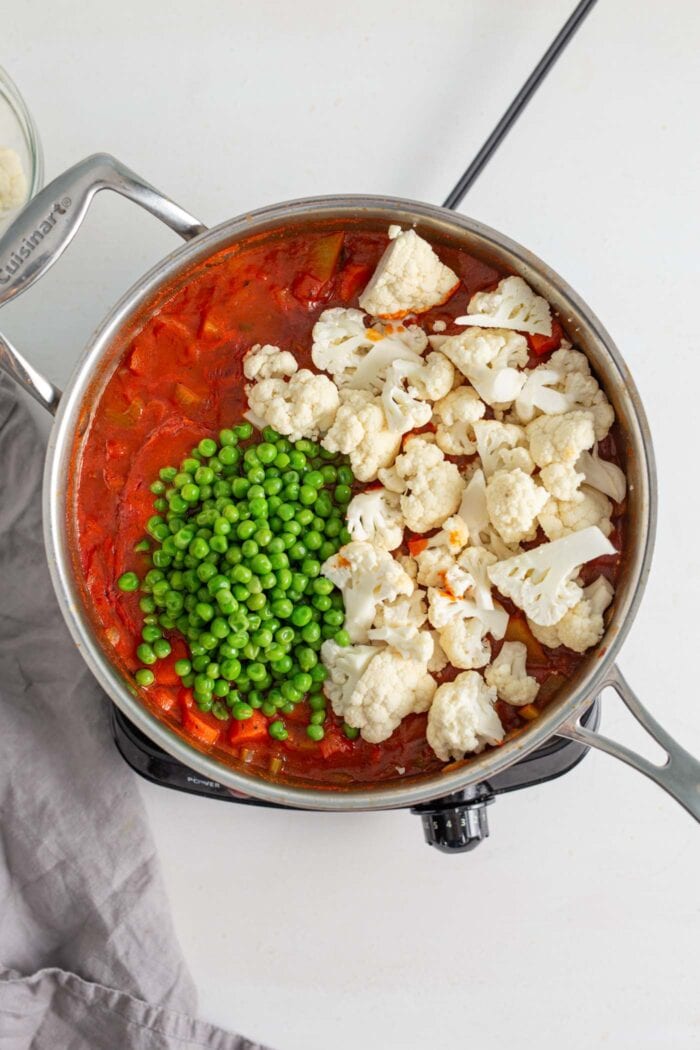 Chopped cauliflower and green peas cooking in a skillet of tomato sauce.