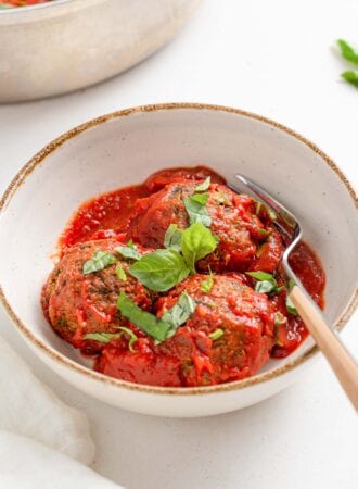 3 lentil meatballs with tomato sauce topped with fresh basil in a bowl.