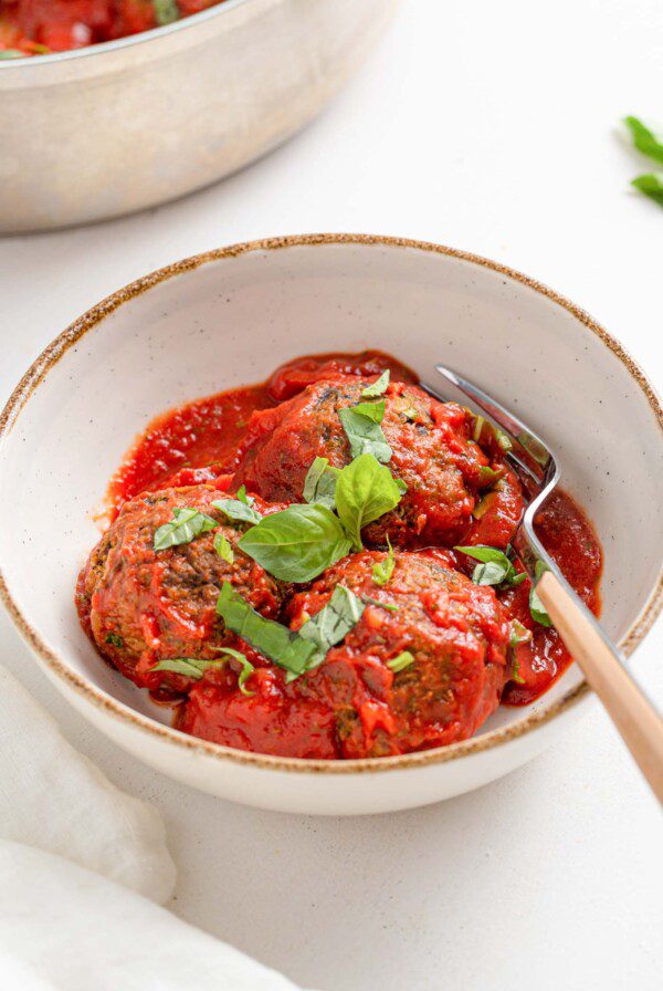 3 lentil meatballs with tomato sauce topped with fresh basil in a bowl.