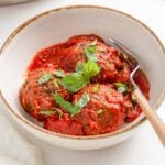 3 lentil meatballs with tomato sauce topped with fresh basil in a bowl.