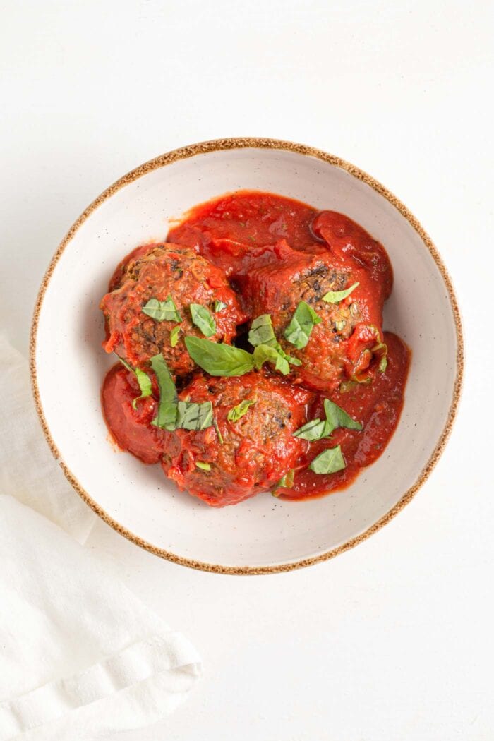 Overhead view of 3 lentil meatballs in a bowl with basil and tomato sauce.