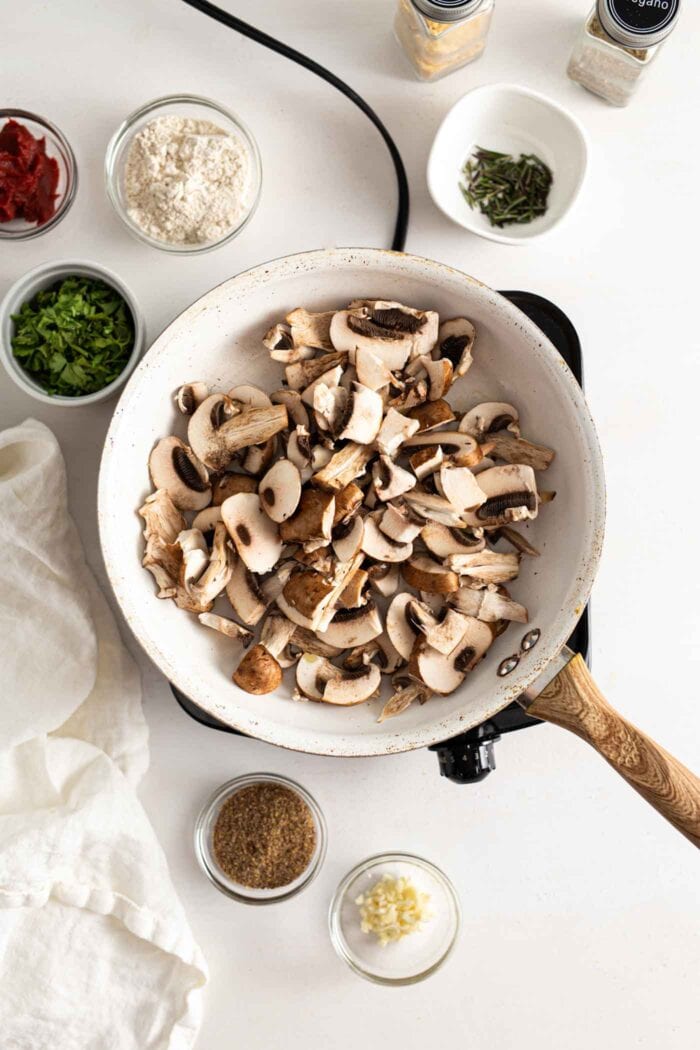 Chopped mushrooms cooking in a skillet on a cook top.