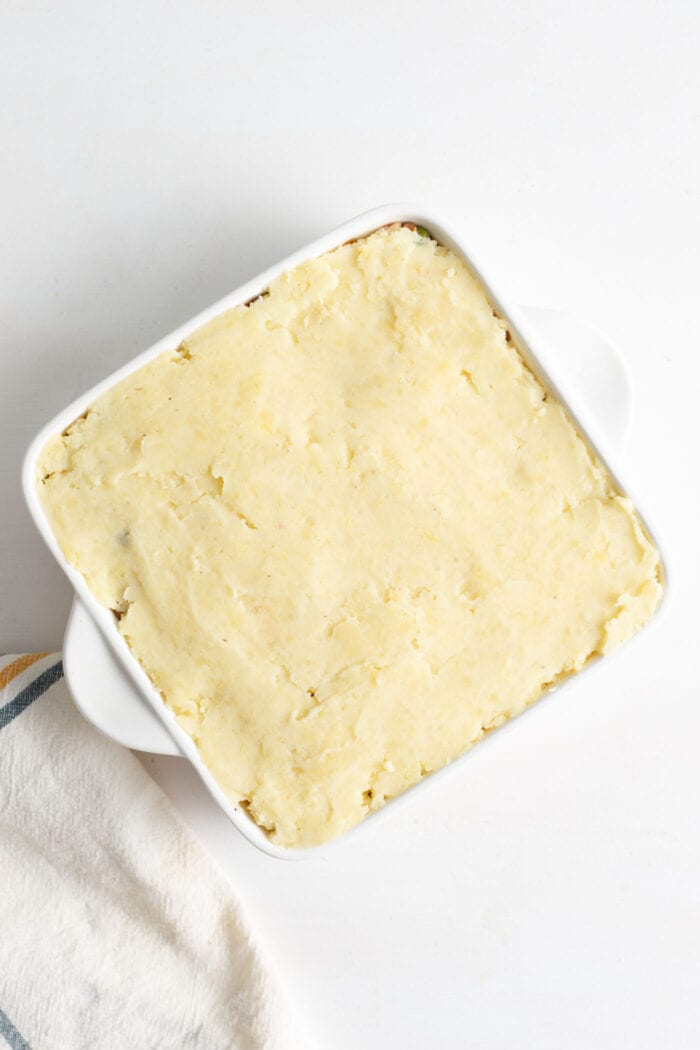 Mashed potatoes evenly spread in a white ceramic baking dish.