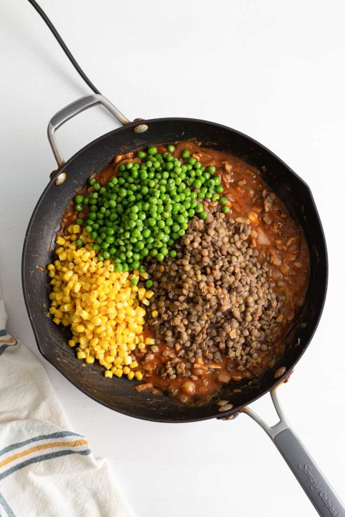 Peas, corn and a cooked vegetable mixture cooking in a skillet.