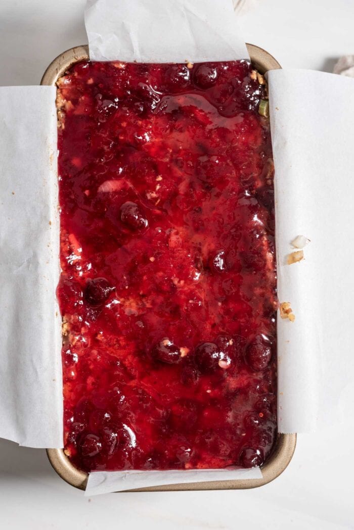 Nut roast topped with whole berry cranberry berry sauce in a loaf in lined with parchment paper.