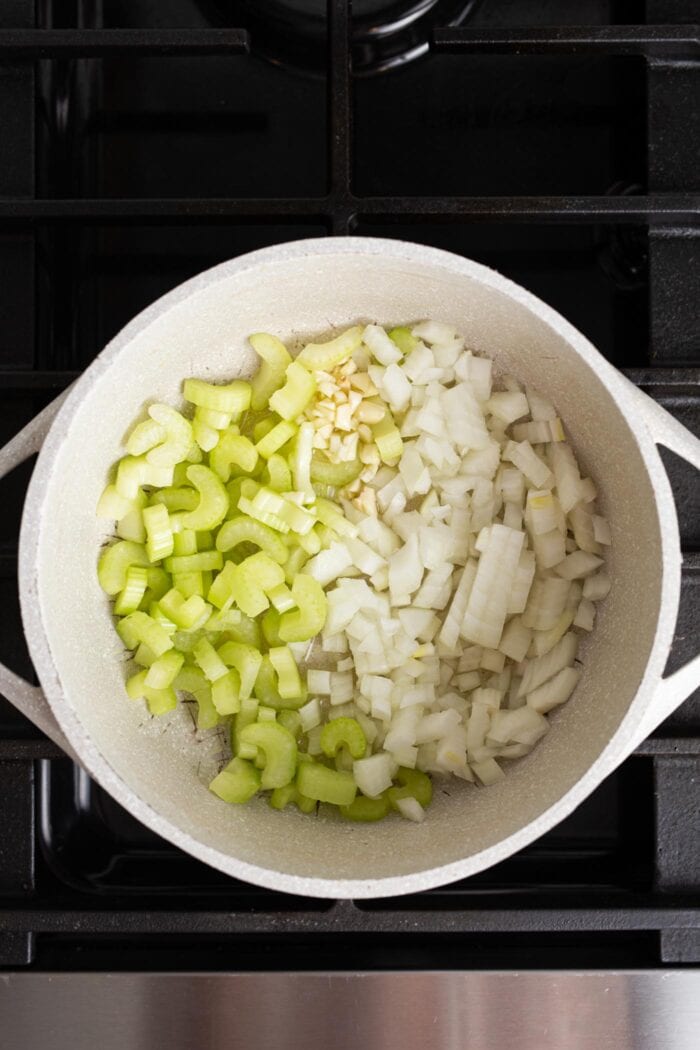 Onions, garlic and celery cooking in a large soup pot on a gas range stove.