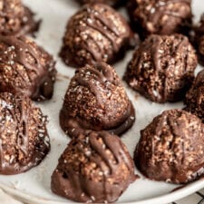 Close up of chocolate coconut macaroons on a white plate sitting on a cooling rack.