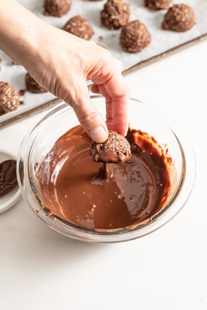 Hand dipping a macaroon into a bowl of melted chocolate.