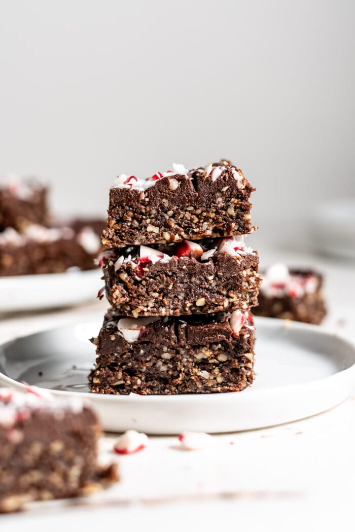 Stack of 3 vegan peppermint brownies topped with ganache and candy canes.