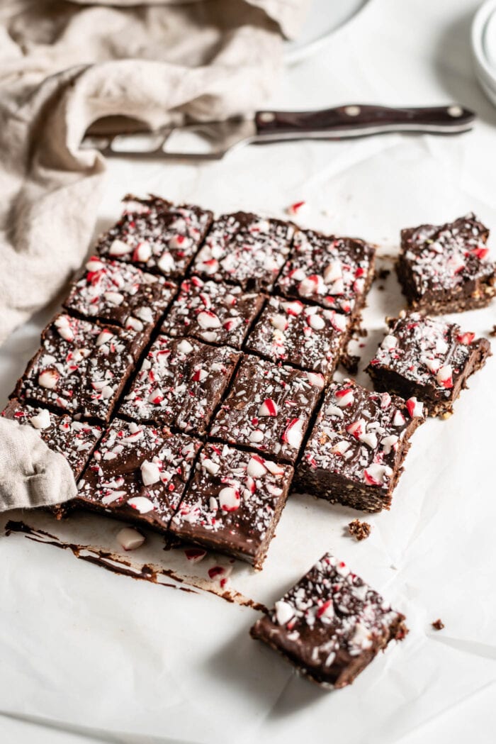 Brownies topped with crushed candy canes cut into 16 squares on a piece of parchment paper.