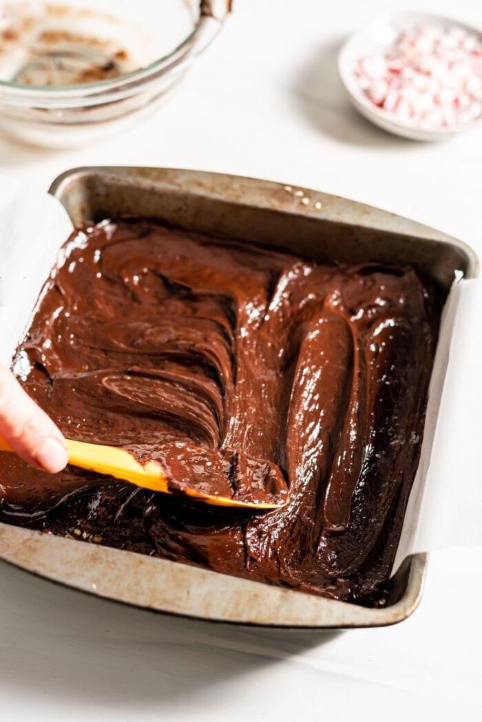 Hand using a spatula to spread melted chocolate in a baking pan.