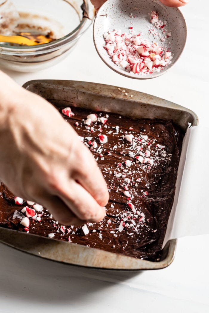 Hand sprinkling crushed candy canes over melted chocolate in a pan.