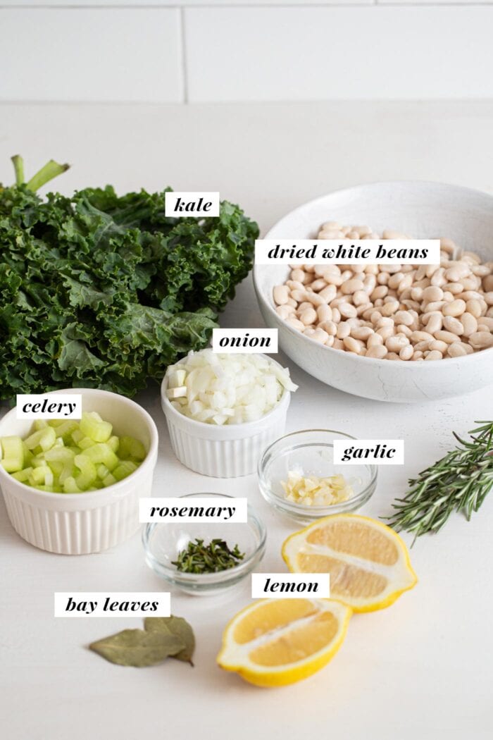Visual of all ingredients needed for making a white bean and kale soup recipes. Ingredients are labelled with text overlay.