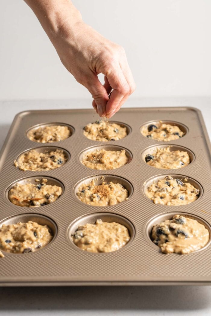 Sprinkling sugar on top of muffin batter in a muffin tin.
