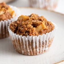 Two applesauce muffins on a plate. More muffins in background.