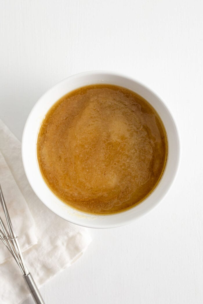Applesauce, maple syrup and coconut oil mixed together in a glass mixing bowl.