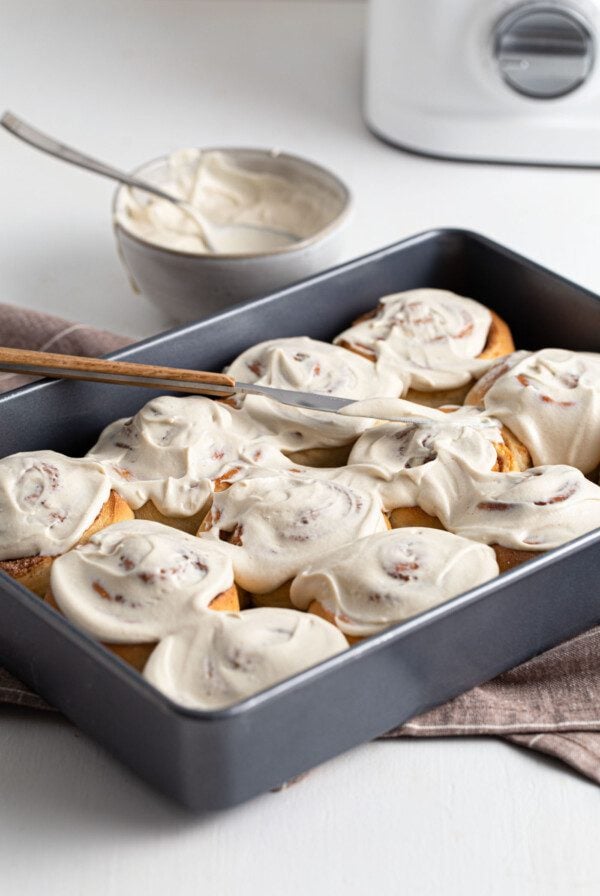 Cinnamon buns spread with frosting in a baking pan.