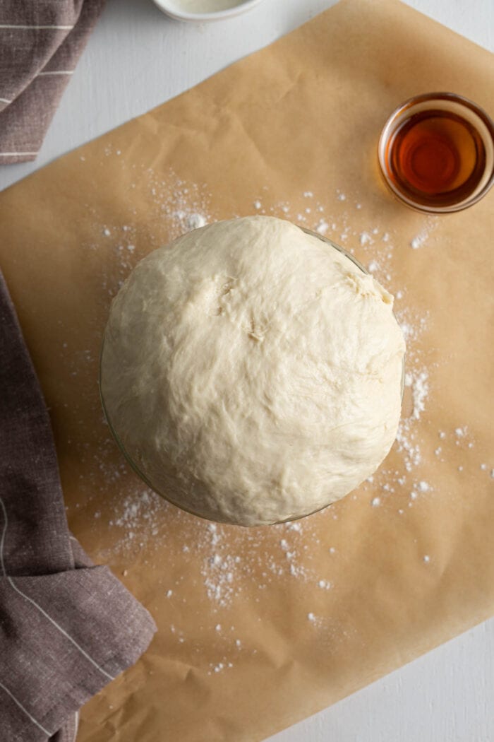 Cinnamon roll dough that has risen into a puffy ball in a bowl.