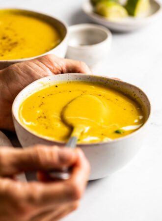 Hand using a spoon to lift a spoonful of squash soup from a bowl.