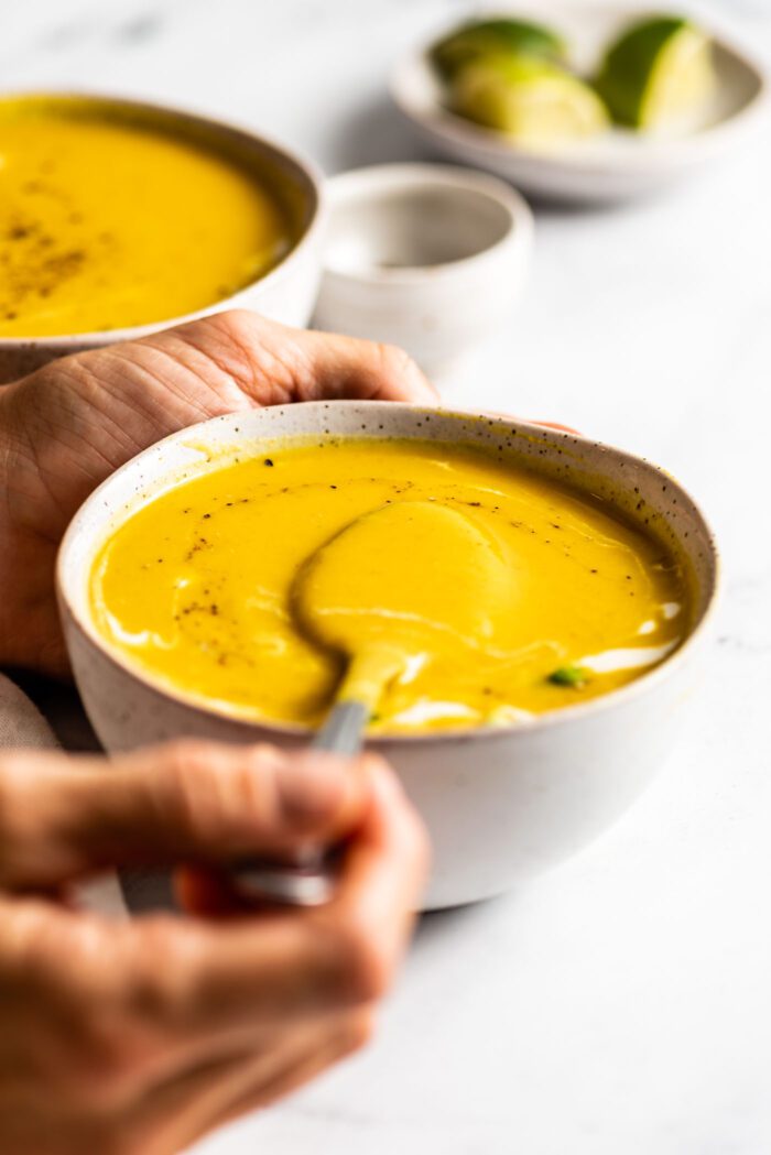 Hand using a spoon to lift a spoonful of squash soup from a bowl.