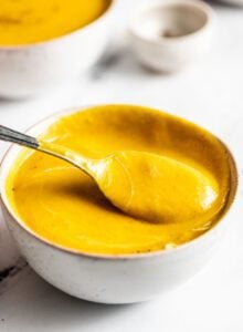 Spoon lifting a spoonful of creamy squash soup from a bowl.