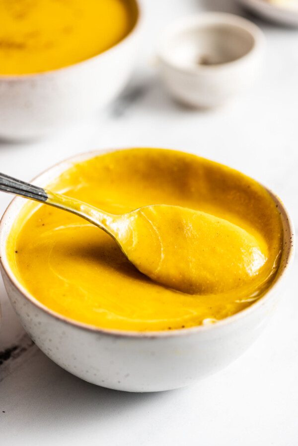 Spoon lifting a spoonful of creamy squash soup from a bowl.