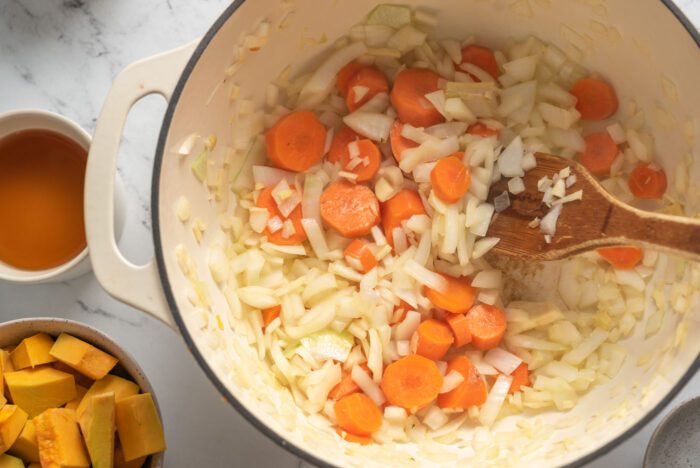 Onion, garlic, ginger and carrots cooking in a large soup pot with a wooden spoon.