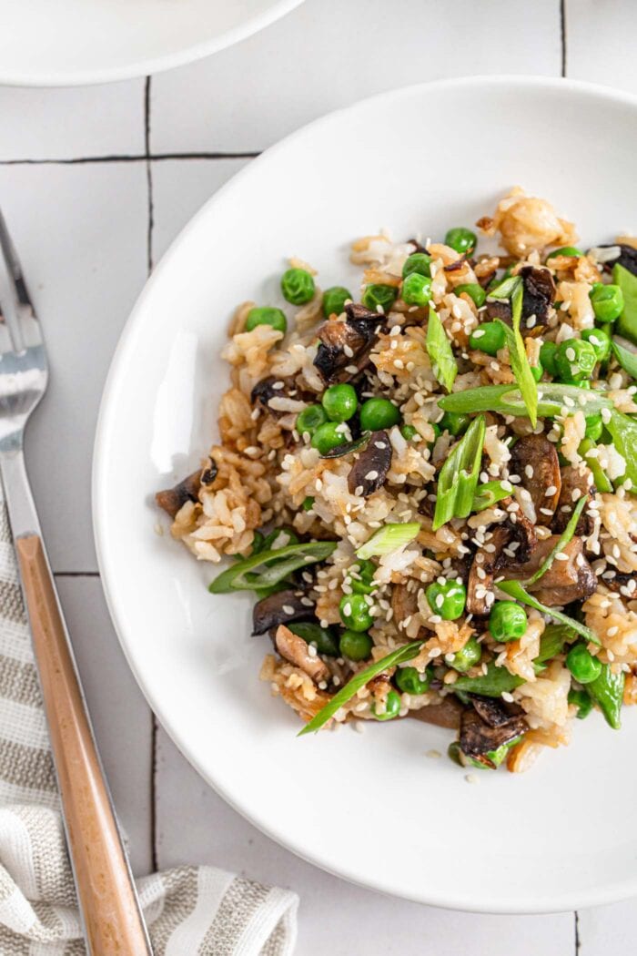 Overhead view of a plate of Chinese mushroom fried rice topped with sesame seeds and spring onions.
