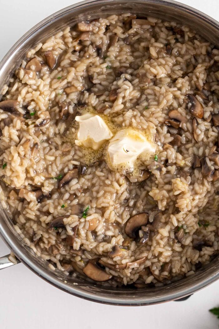 Close up of creamy vegan mushroom risotto topped with butter in a large pot.