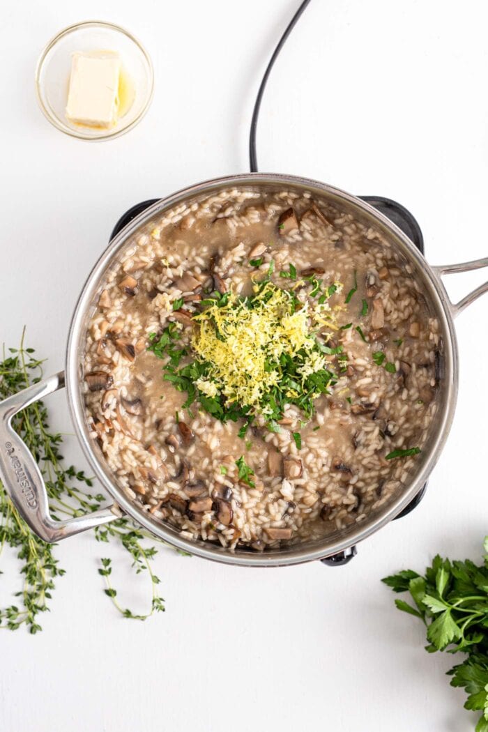 Skillet of mushroom risotto topped with lemon zest and fresh chopped parsley.