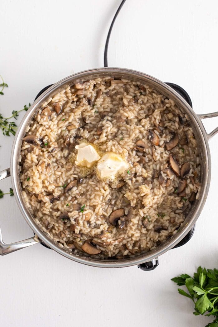 Large pot of creamy vegan mushroom risotto topped with butter. Some parsley is beside the pot.