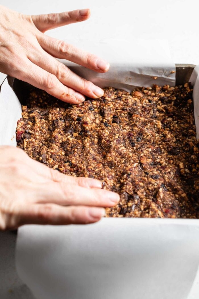 Two hands pressing raw energy bar dough into a baking pan.