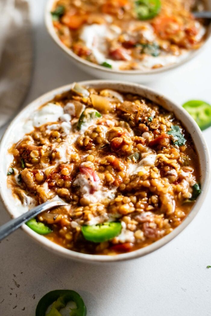 Bowl of lentil chili topped with sour cream and jalapeno. Spoon rests in bowl.