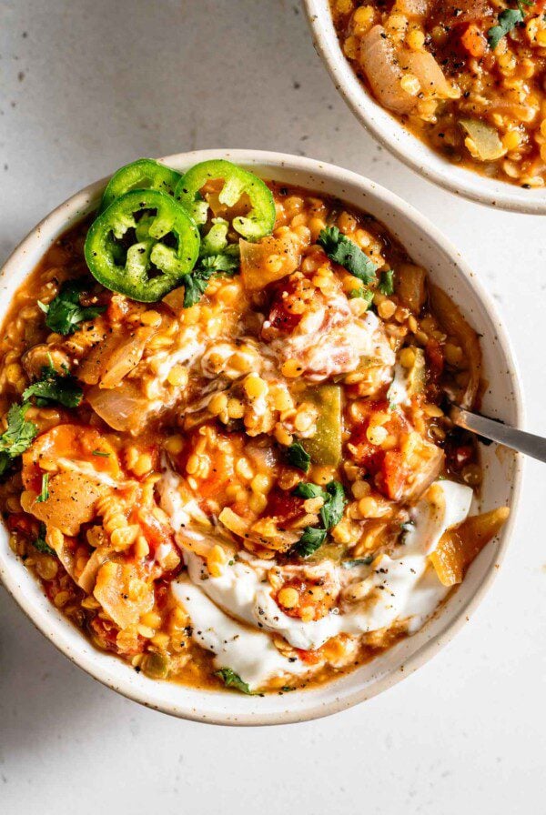 Overhead view of a a bowl of lentil chili with sour cream and jalapeños on top.