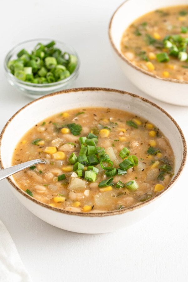 Bowl of white chili topped with sliced scallions.