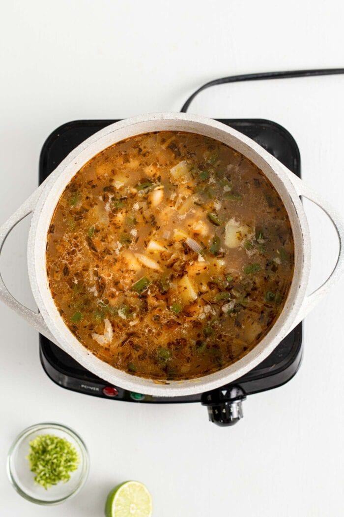 Soup with beans and potato cooking in a large pot on a small induction cook top.