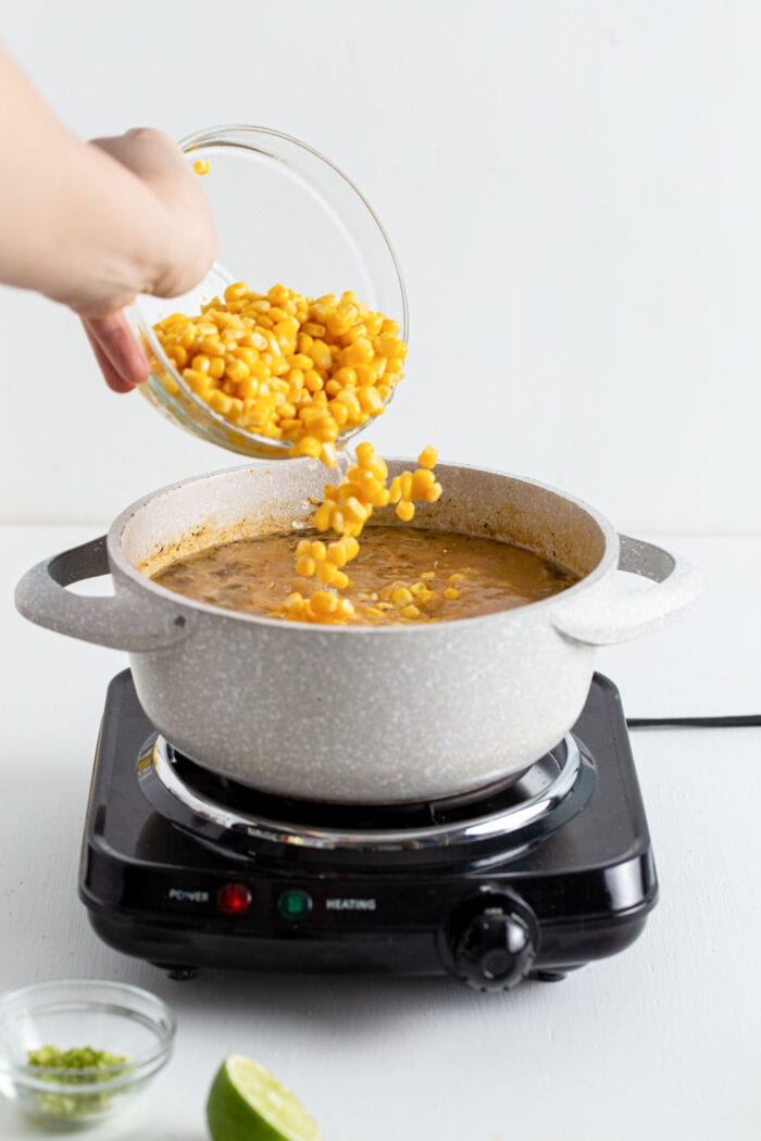Adding a bowl of corn to chili cooking in a large pot.