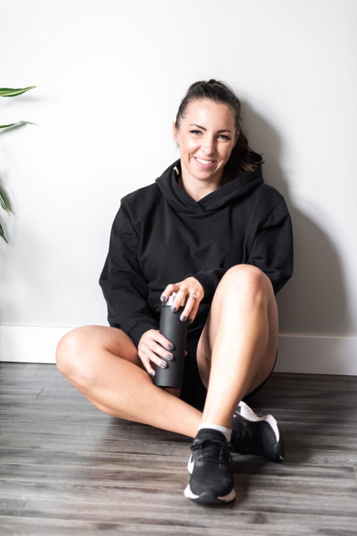 Woman in athletic gear sitting against a wall holding a water bottle.