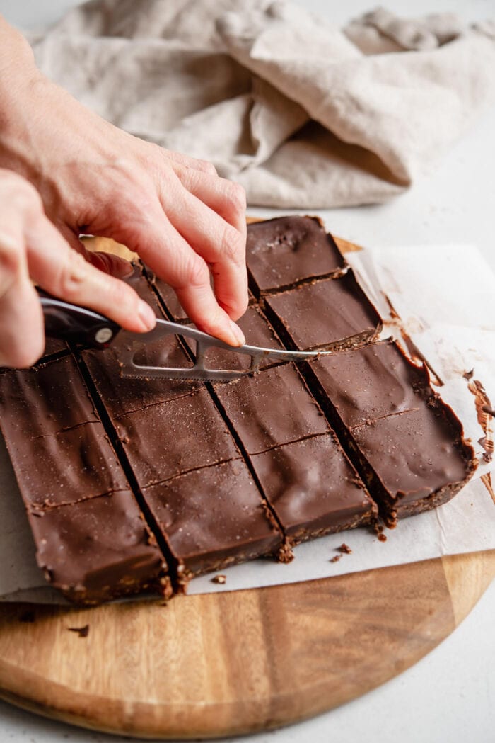 Hands using a knife to slice chocolate bars into squares.