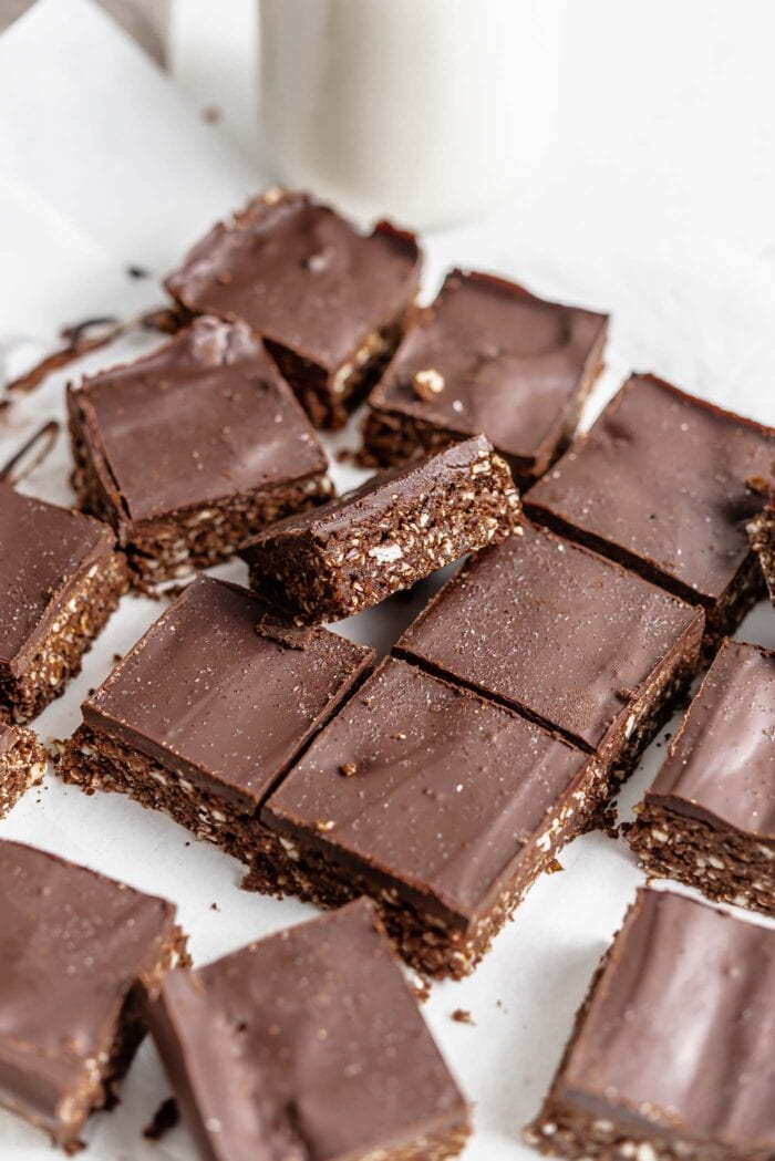 Many no-bake chocolate almond squares scattered on a piece of parchment paper.