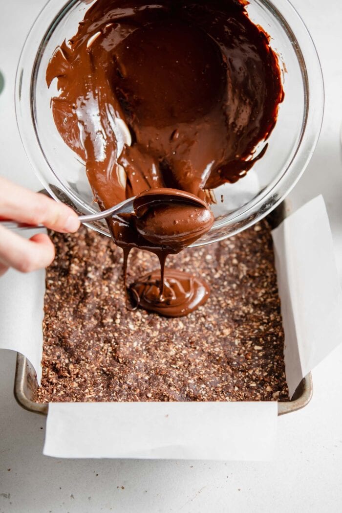 Pouring melted chocolate over chocolate bars in a baking pan.