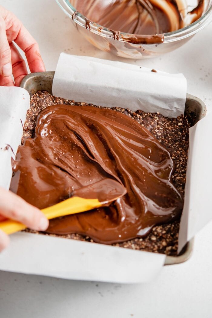 Using a spatula to spread melted chocolate over bars in a baking dish.