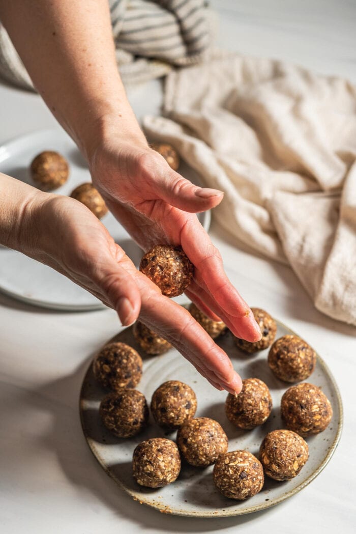 Two hands rolling energy ball dough into balls.